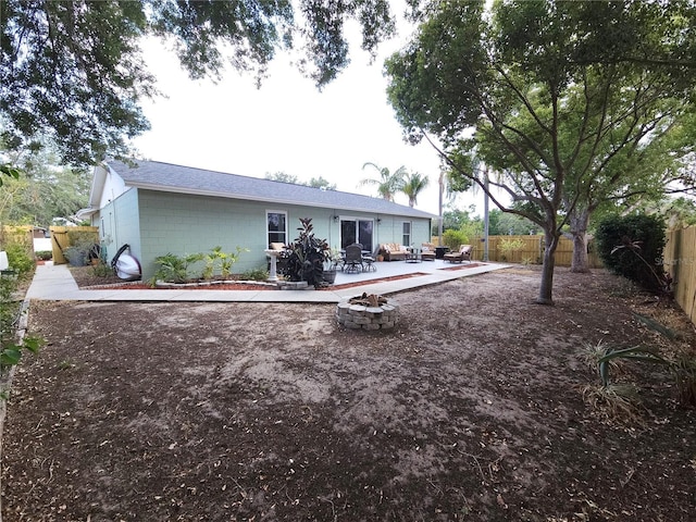 back of property with concrete block siding, a patio, a fenced backyard, and a fire pit