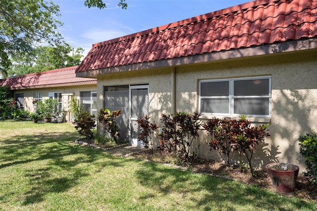 view of property exterior with a tiled roof, a lawn, and stucco siding