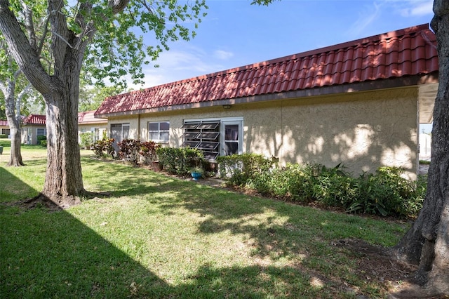view of property exterior with a yard, stucco siding, and a tiled roof