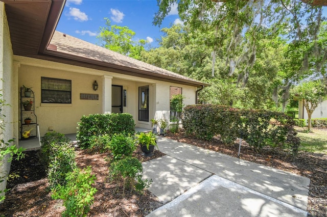 view of exterior entry featuring covered porch, a shingled roof, and stucco siding