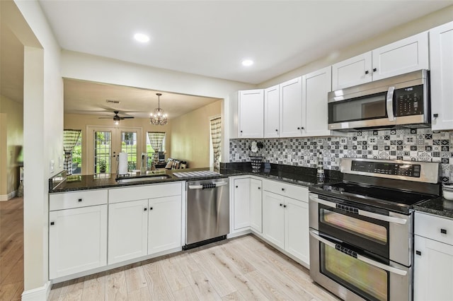 kitchen with a sink, stainless steel appliances, white cabinetry, decorative backsplash, and light wood-type flooring
