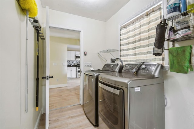 clothes washing area featuring baseboards, laundry area, light wood-type flooring, and washing machine and clothes dryer