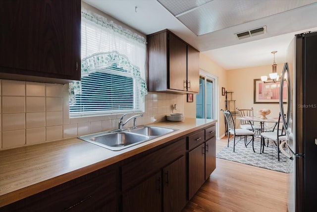 kitchen with a sink, visible vents, freestanding refrigerator, dark brown cabinetry, and light wood-type flooring