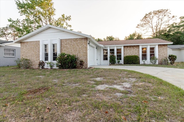 ranch-style home with a garage, a front yard, driveway, and stone siding