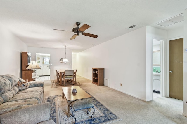living area featuring light colored carpet, visible vents, a ceiling fan, and baseboards