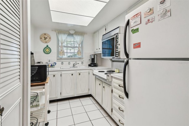 kitchen featuring white appliances, light countertops, white cabinets, a sink, and light tile patterned flooring