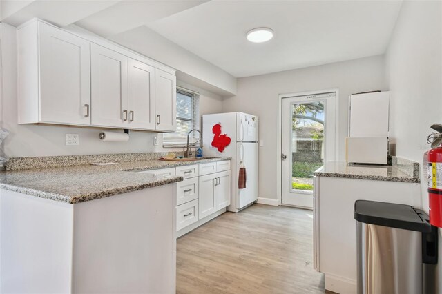 kitchen with white cabinetry, a sink, light wood finished floors, and freestanding refrigerator