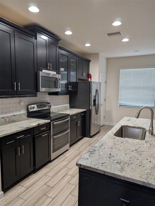 4697 Wandering Way, Wesley Chapel, FL 33544 - kitchen with stainless steel appliances, a sink, dark cabinetry, decorative backsplash, and light wood-type flooring
