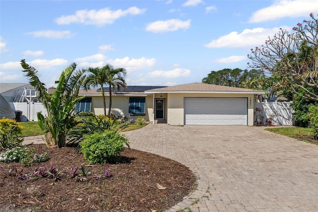 ranch-style home featuring fence, driveway, solar panels, and stucco siding