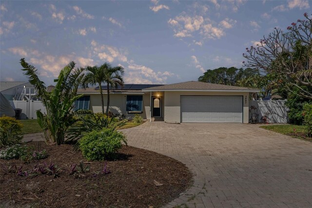 single story home featuring a garage, fence, stucco siding, roof mounted solar panels, and driveway