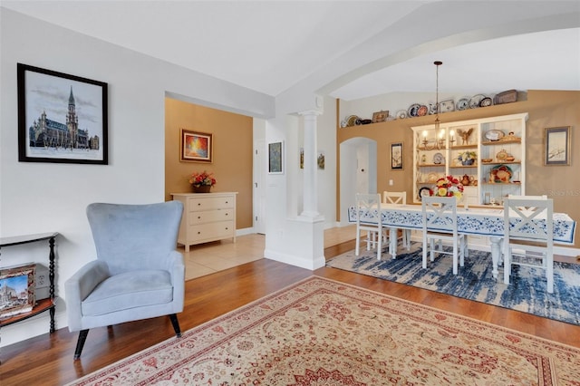 sitting room featuring arched walkways, wood finished floors, decorative columns, a notable chandelier, and lofted ceiling