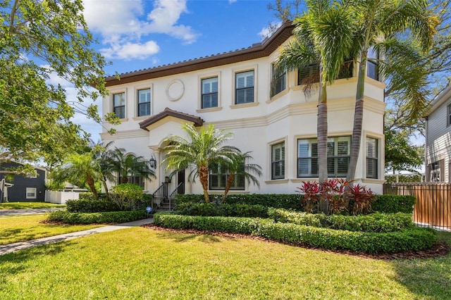 mediterranean / spanish-style house with stucco siding, fence, and a front lawn