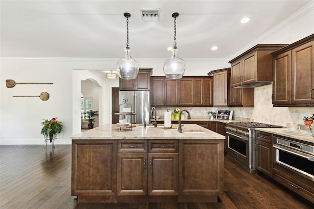 kitchen featuring a sink, premium appliances, visible vents, an island with sink, and backsplash
