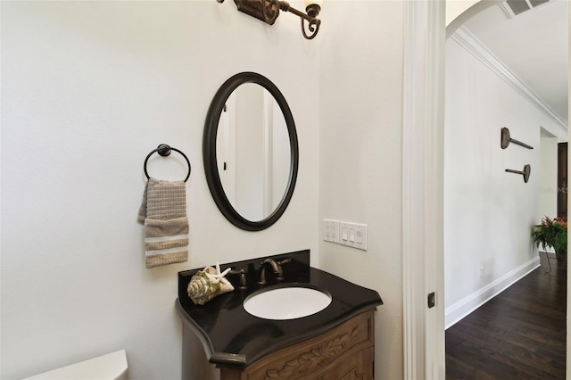 bathroom with wood finished floors, vanity, baseboards, visible vents, and crown molding