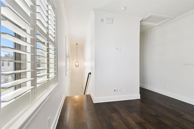 empty room with dark wood-type flooring, attic access, crown molding, and baseboards