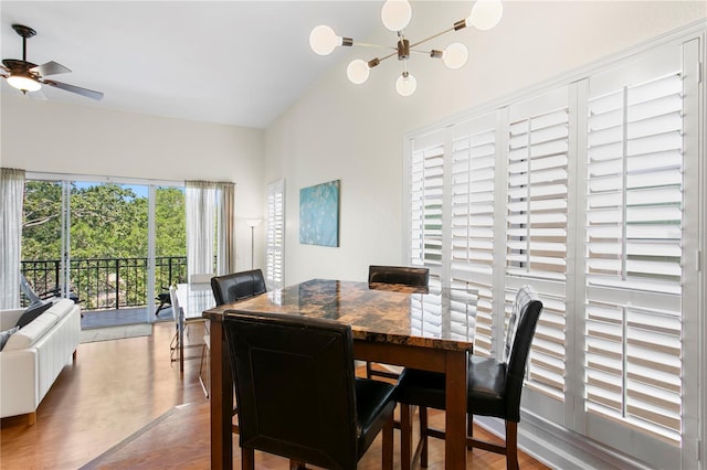 dining space with ceiling fan with notable chandelier, wood finished floors, and vaulted ceiling