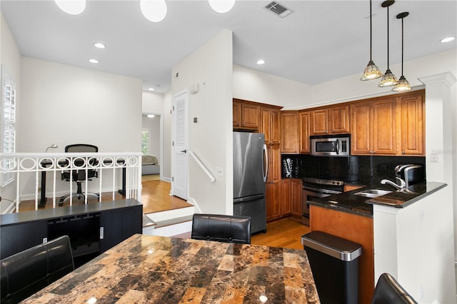 kitchen featuring brown cabinets, appliances with stainless steel finishes, a sink, light wood-style floors, and visible vents