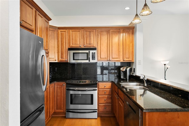 kitchen featuring brown cabinets, a sink, a peninsula, dark stone counters, and stainless steel appliances