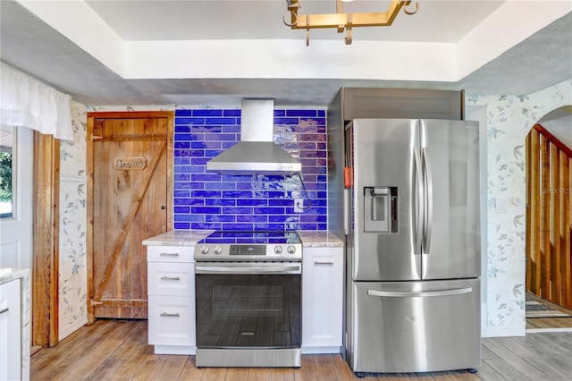 kitchen with stainless steel appliances, light wood-type flooring, white cabinetry, wall chimney range hood, and wallpapered walls