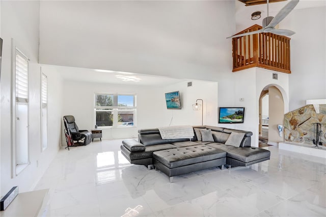 living area featuring a towering ceiling, marble finish floor, arched walkways, and a ceiling fan