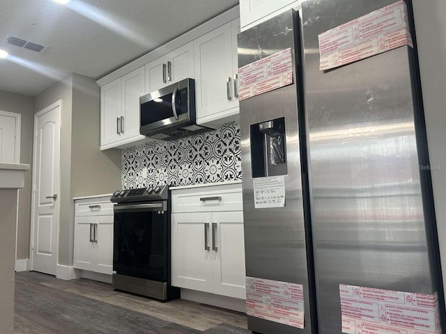 kitchen featuring white cabinetry, decorative backsplash, appliances with stainless steel finishes, visible vents, and dark wood-style floors