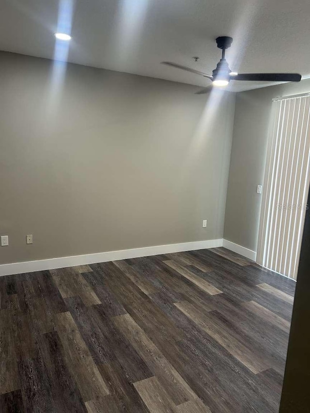 spare room featuring a ceiling fan, dark wood-style floors, and baseboards