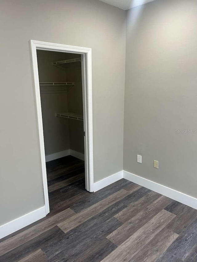 unfurnished bedroom featuring a closet, dark wood-style floors, and baseboards
