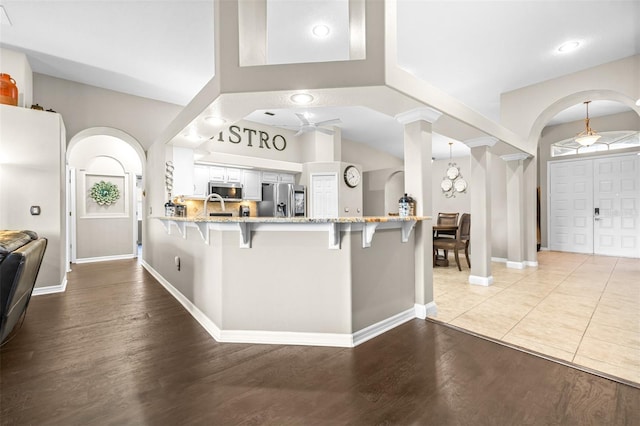 kitchen with appliances with stainless steel finishes, light stone counters, a kitchen breakfast bar, and arched walkways