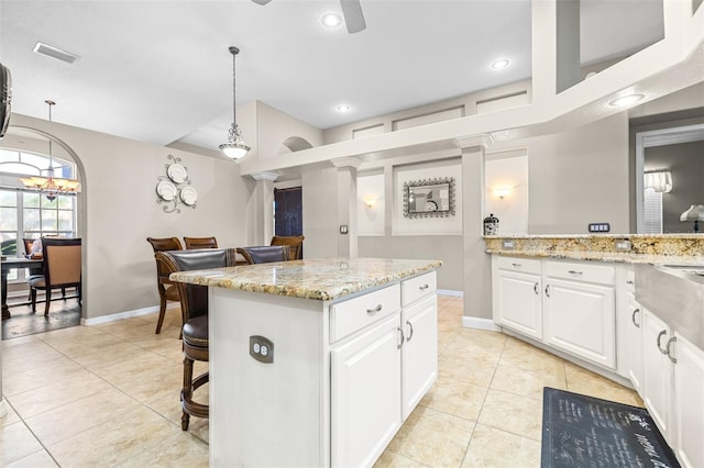 kitchen with light tile patterned floors, white cabinets, ceiling fan, a kitchen bar, and a center island
