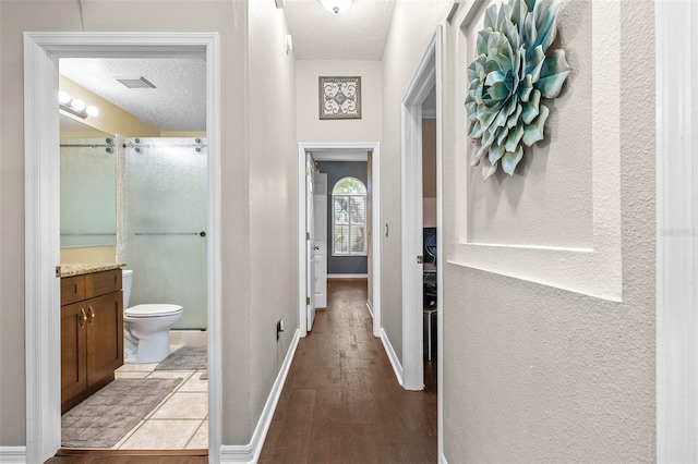 hall featuring light wood-style floors, a textured wall, baseboards, visible vents, and a textured ceiling