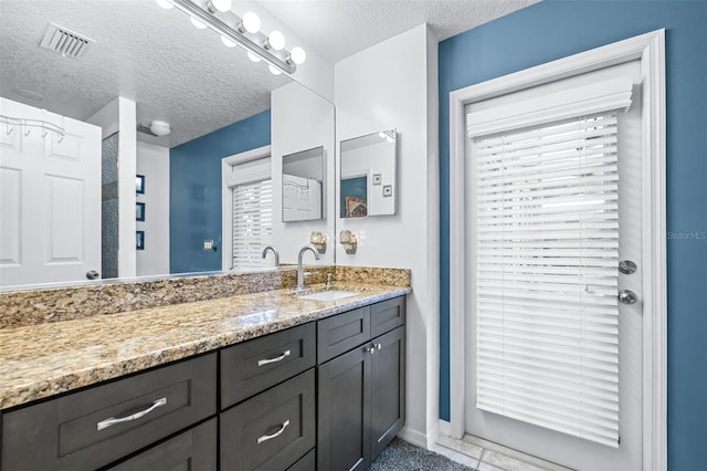bathroom featuring baseboards, visible vents, a textured ceiling, and vanity