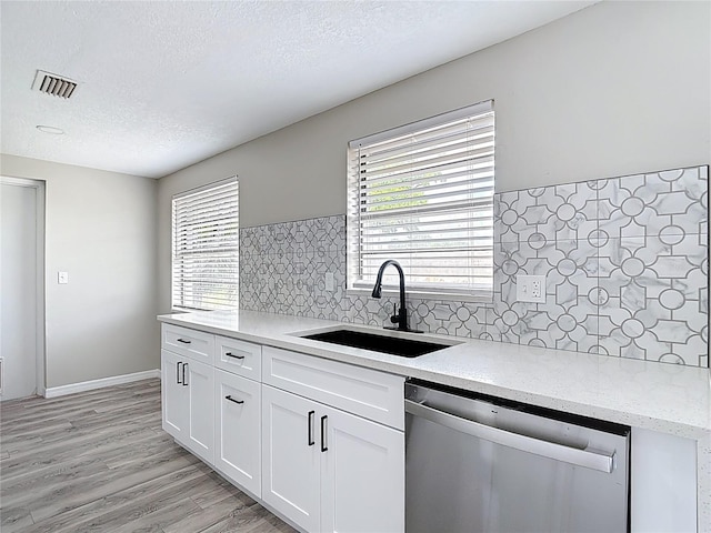 kitchen with a textured ceiling, dishwasher, a sink, light stone counters, and white cabinets