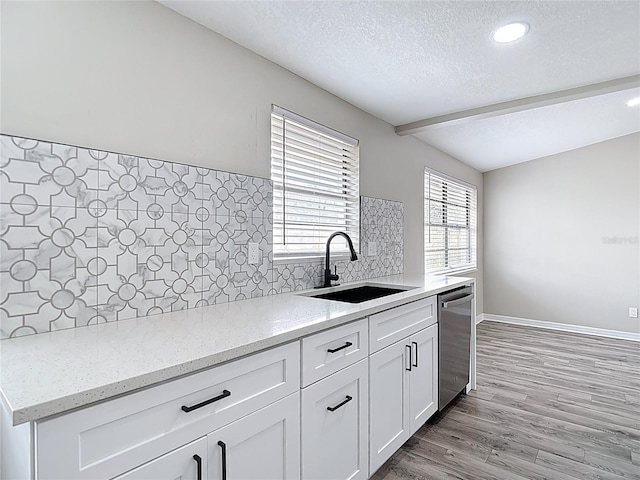 kitchen featuring a textured ceiling, light stone counters, a sink, light wood finished floors, and dishwasher