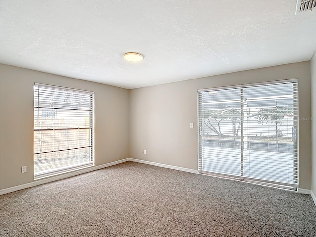 carpeted empty room with baseboards, a textured ceiling, and visible vents
