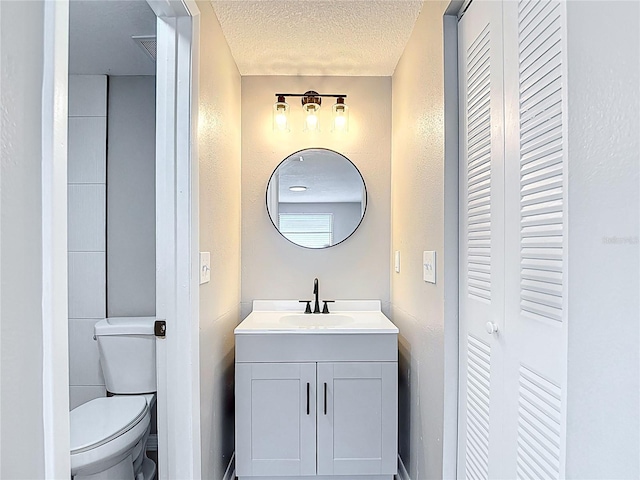 bathroom featuring vanity, a textured ceiling, a textured wall, and toilet