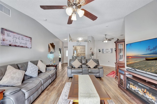 living room with visible vents, lofted ceiling, light wood-style floors, ceiling fan, and a textured ceiling