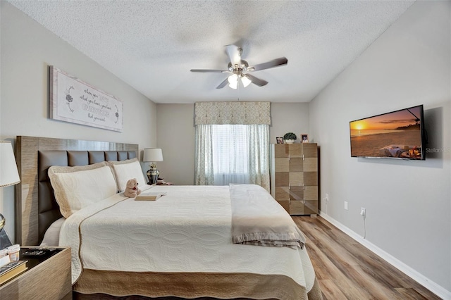 bedroom with a textured ceiling, baseboards, a ceiling fan, and wood finished floors