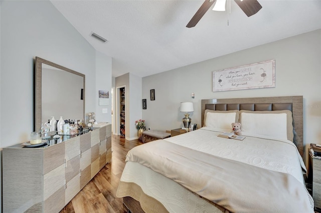 bedroom featuring a ceiling fan, visible vents, wood finished floors, and vaulted ceiling