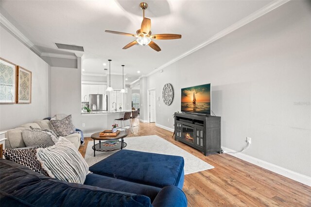 living room featuring crown molding, ceiling fan, light wood-style floors, baseboards, and visible vents