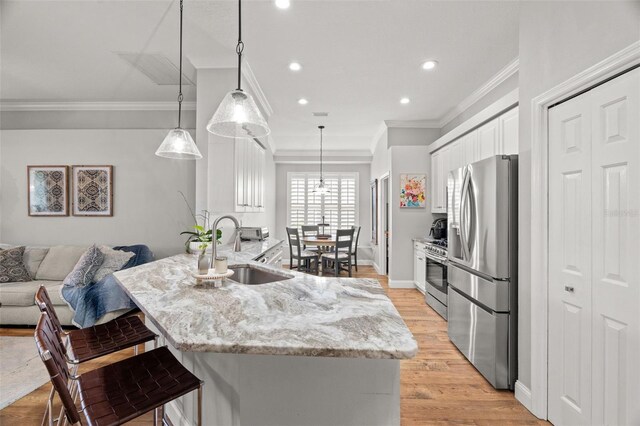 kitchen featuring appliances with stainless steel finishes, light stone counters, a sink, white cabinetry, and ornamental molding