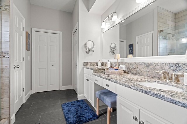 full bathroom with double vanity, a tile shower, a sink, baseboards, and a closet