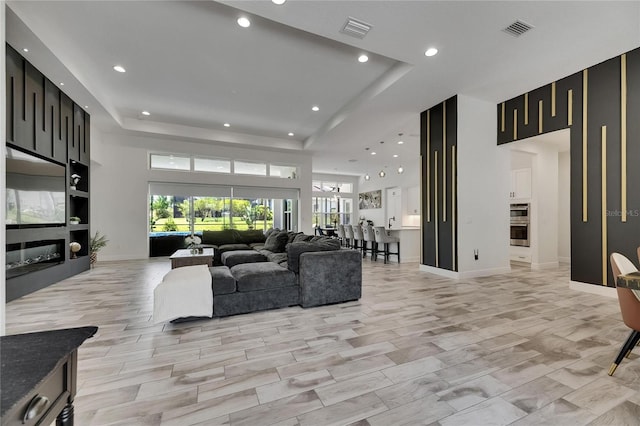living room with a tray ceiling, visible vents, a healthy amount of sunlight, and a high end fireplace