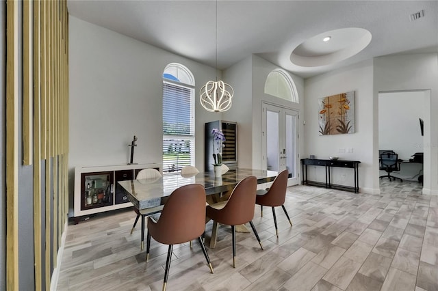dining space featuring visible vents, a towering ceiling, baseboards, light wood-type flooring, and french doors