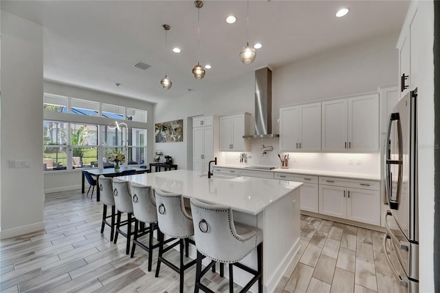 kitchen featuring visible vents, freestanding refrigerator, wall chimney range hood, light countertops, and black electric cooktop