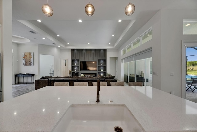 kitchen featuring visible vents, open floor plan, a raised ceiling, light stone counters, and hanging light fixtures