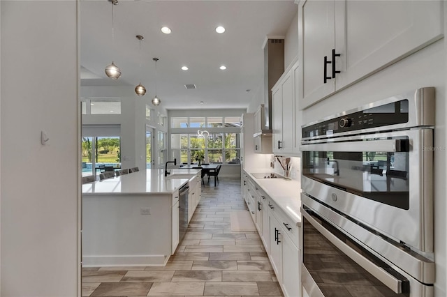 kitchen featuring appliances with stainless steel finishes, a kitchen island with sink, light countertops, recessed lighting, and white cabinetry