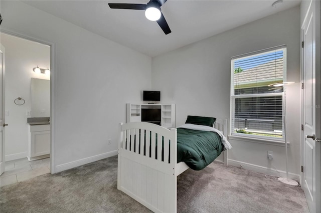 bedroom featuring baseboards, ensuite bathroom, a ceiling fan, and light colored carpet