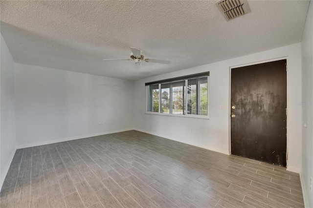 spare room featuring a textured ceiling, a ceiling fan, wood finished floors, and visible vents
