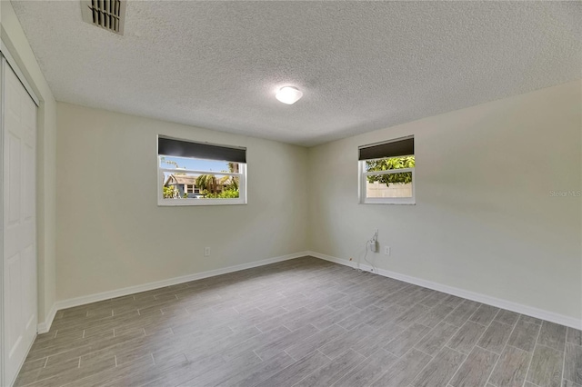 empty room featuring visible vents, baseboards, wood finished floors, and a wealth of natural light
