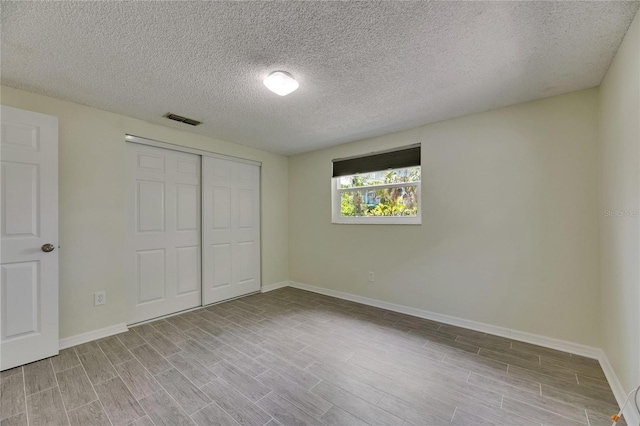 unfurnished bedroom with a textured ceiling, baseboards, wood finished floors, visible vents, and a closet